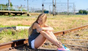 Lonely and sad teenager girl sitting on rusty rail track in the countryside. Adolescence problems